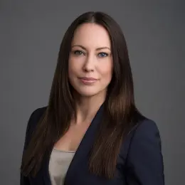 Professional headshot of Anne Brockland wearing business attire, against a plain grey background.