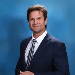 Professional headshot of Chandler Gregg wearing business attire, against a plain grey background.