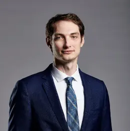 Professional headshot of Jacob Lewis wearing business attire, against a plain grey background.