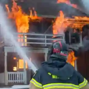 A firefighter extinguishing a fierce blaze engulfing a residential home, illustrating product liability issues related to fire safety.