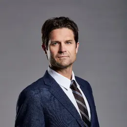 Professional headshot of Chandler Gregg wearing business attire, against a plain grey background.